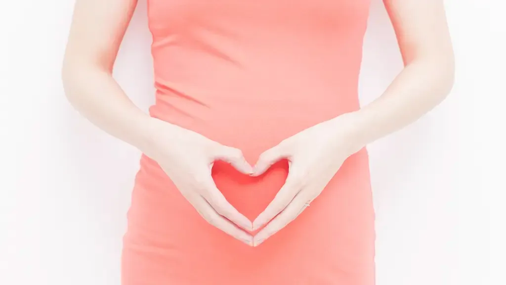 オレンジ色のワンピースを着てお腹の前でハートを作る