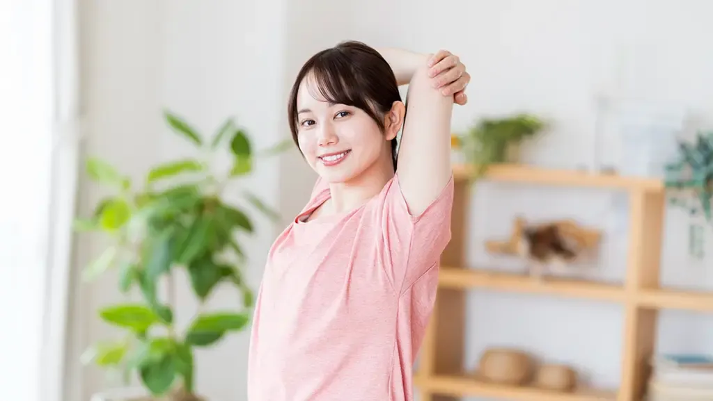 ピンクの半袖の女性が腕と肩をほぐしている