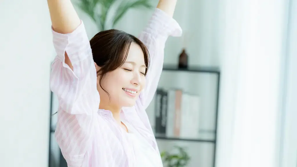 淡いピンクのシャツを着て腕を上に伸ばしている